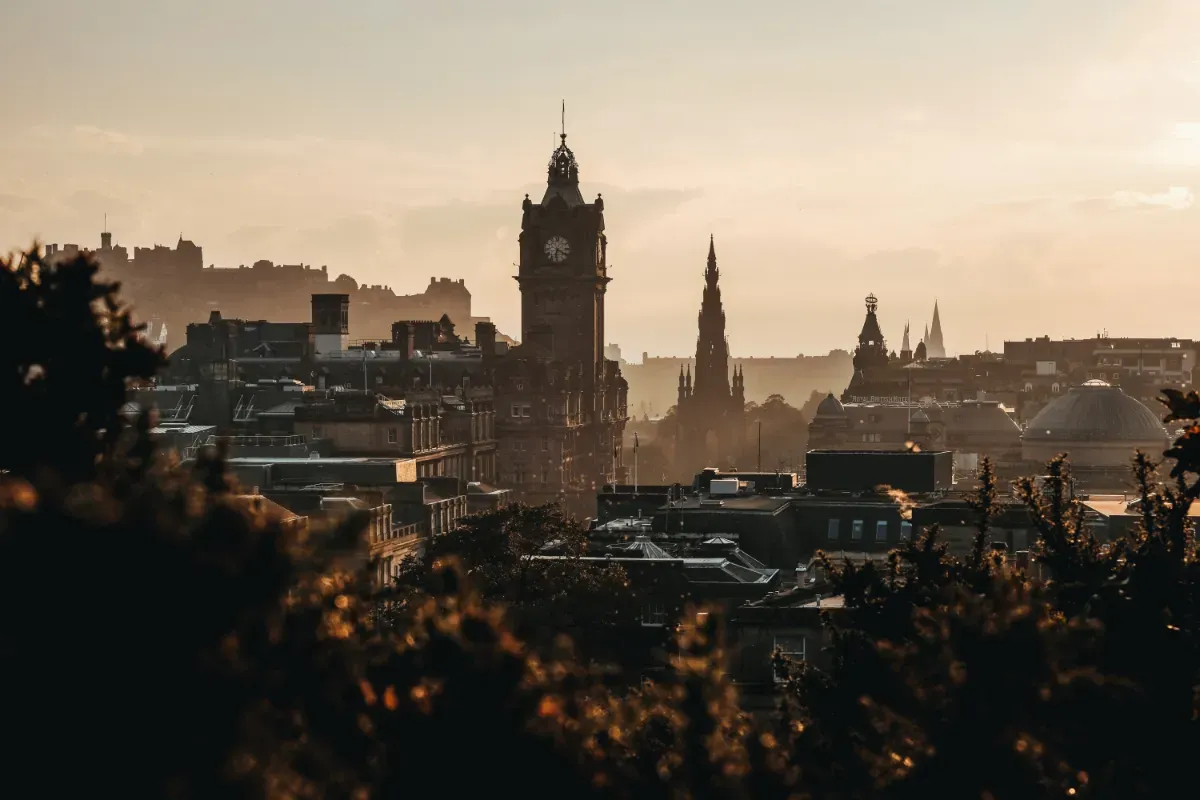 A view over Edinburgh from Calton Hill. The sun is low in the sky casting golden light over the buildings and spires. 