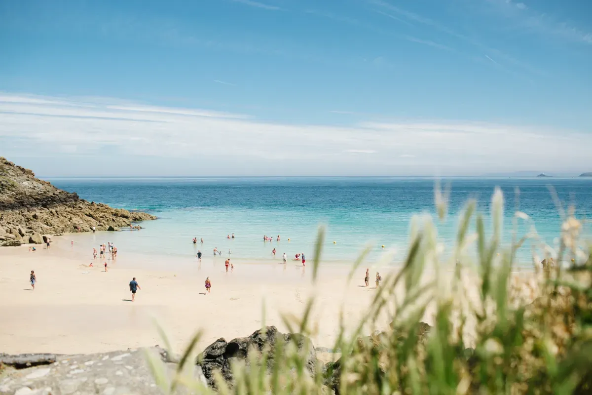 People enjoying the sunshine on St Ives beach in Cornwall, with golden sand and blue sky and sea. 