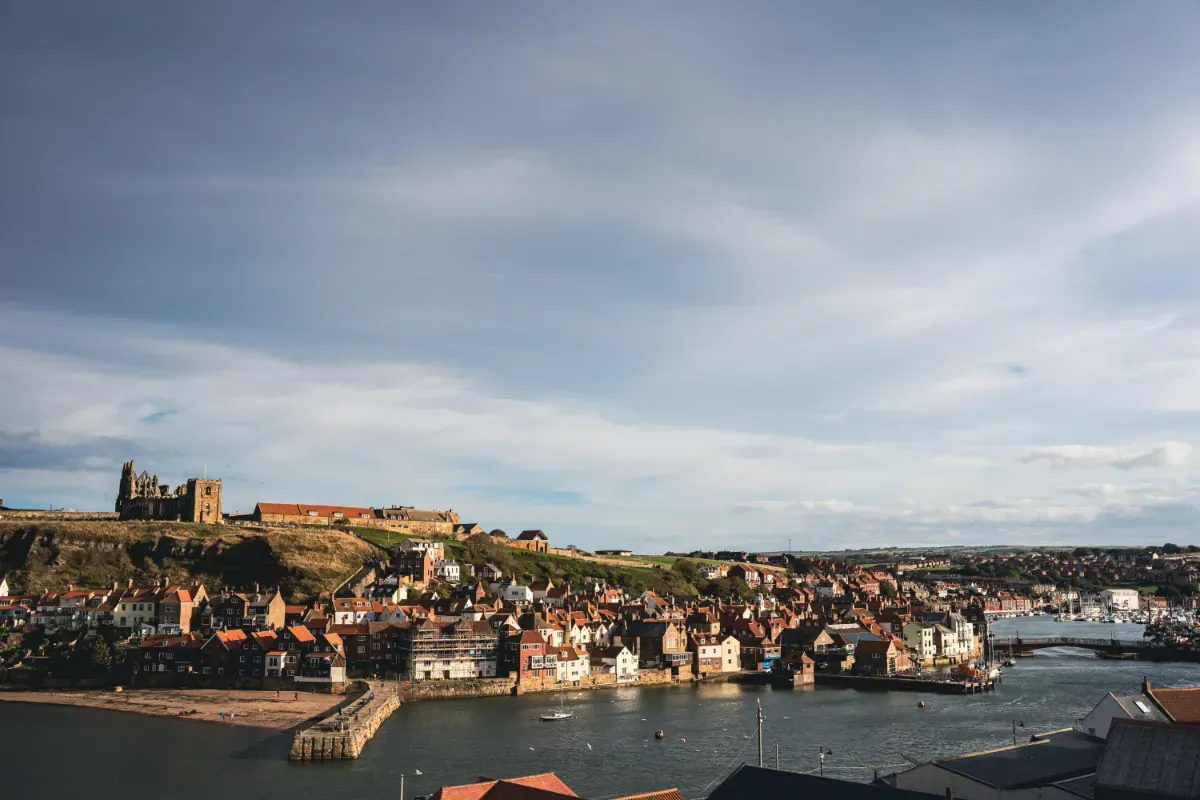 A view over Whitby Harbour, showing Whitby Abbey, the Whitby Swing Bridge over the River Esk and higgledy-piggledy houses next to the river. 