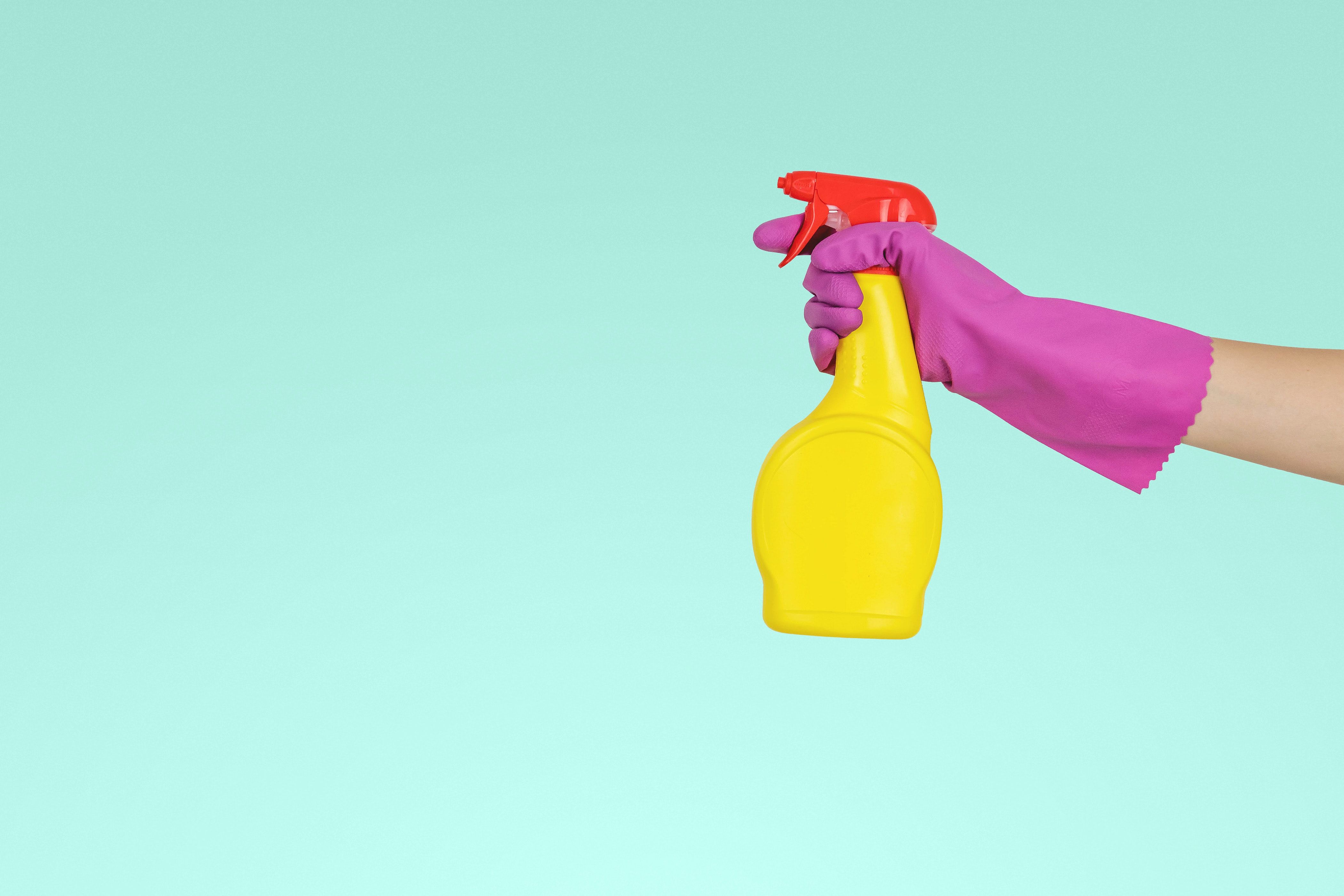 Hand in pink cleaning glove holding yellow cleaning spray