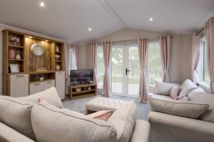 The Willerby Sheraton lounge has two freestanding grey sofas with a matching grey footstool, with peach colours soft furnishings to match the colour scheme.