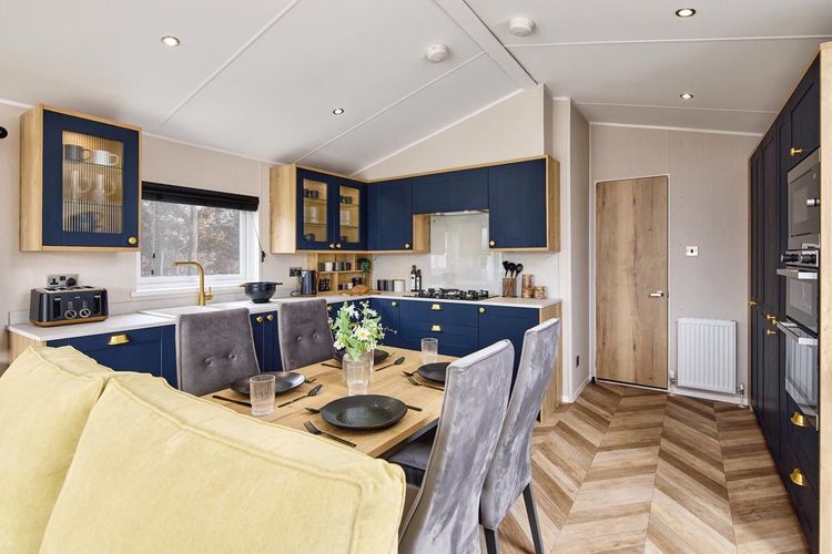 The Willerby Gainsborough contemporary kitchen with a dining oak effect table and grey chairs, and has zig-zag wooden flooring.