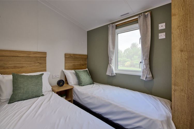 The Willerby Ellerton Extra twin bedroom has oak effect storage units and a green accent wall with matching soft furnishings.