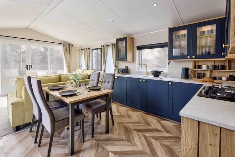 The Willerby Gainsborough luxurious kitchen is equipped with blue cabinet doors and gold accents, topped with a white marble effect worktop.