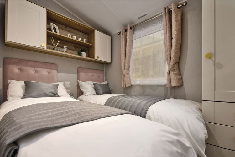 The Willerby Sierra twin bedroom has oak effect storage units with white cupboard doors, and pink upholstered headboards and matching curtains.