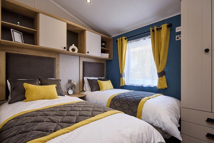 The Willerby Gainsborough twin bedroom is surrounded by storage with grey and yellow soft furnishings.