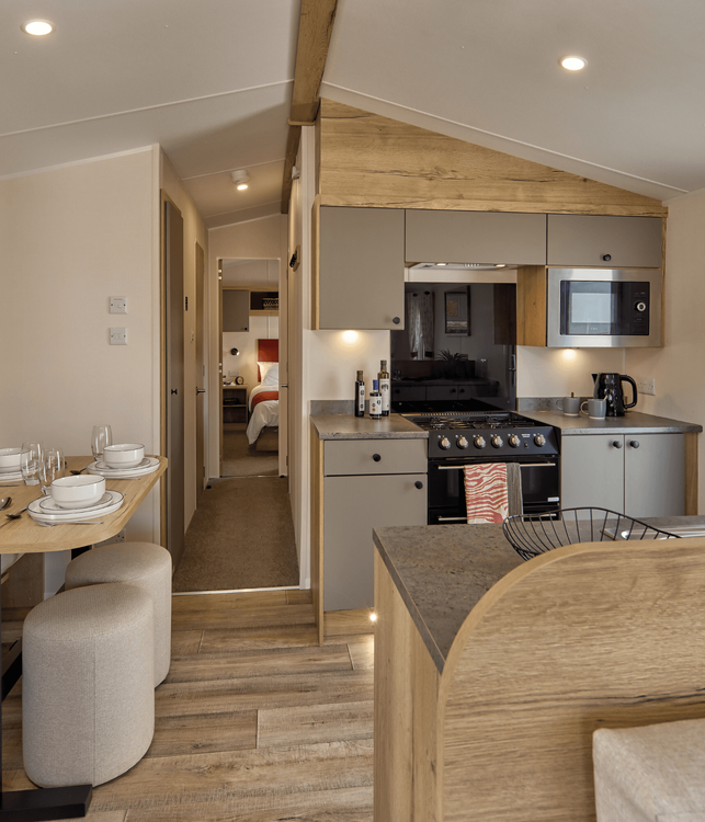 The Willerby Rio kitchen and dining area has oak effect kitchen storage units with light grey cupboards and worktops, and the dining area has an oak effect acoustic accent wall.