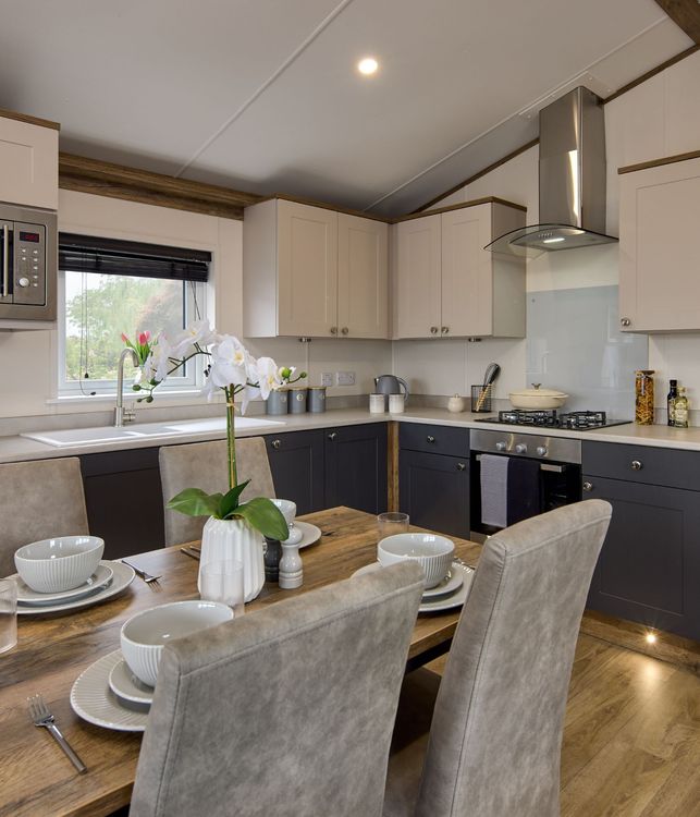 The Willerby Malton Elite kitchen has a dark oak effect dining table with grey seating, and dark grey and cream cupboard doors matching the homes colour scheme.