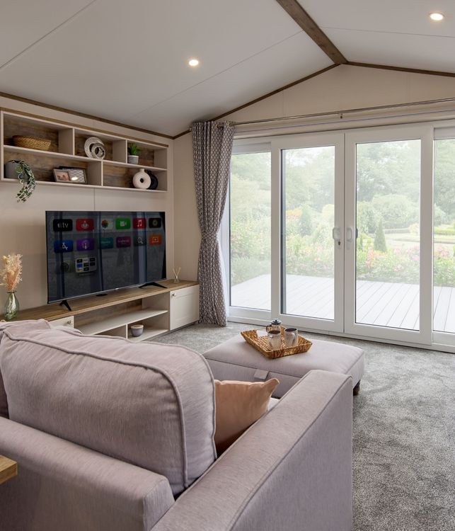 The Willerby Malton Elite spacious lounge with two grey free-standing sofas and a matching footstool with a storage media unit in cream and a dark oak effect.