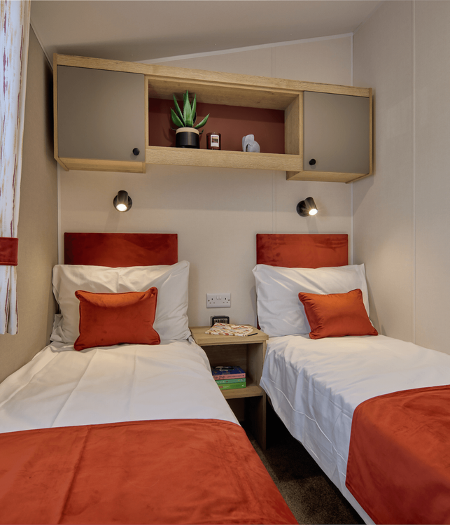 The Willerby Rio twin bedroom with orange soft furnishings and an oak effect storage unit with grey cupboard doors, matching the master bedroom.