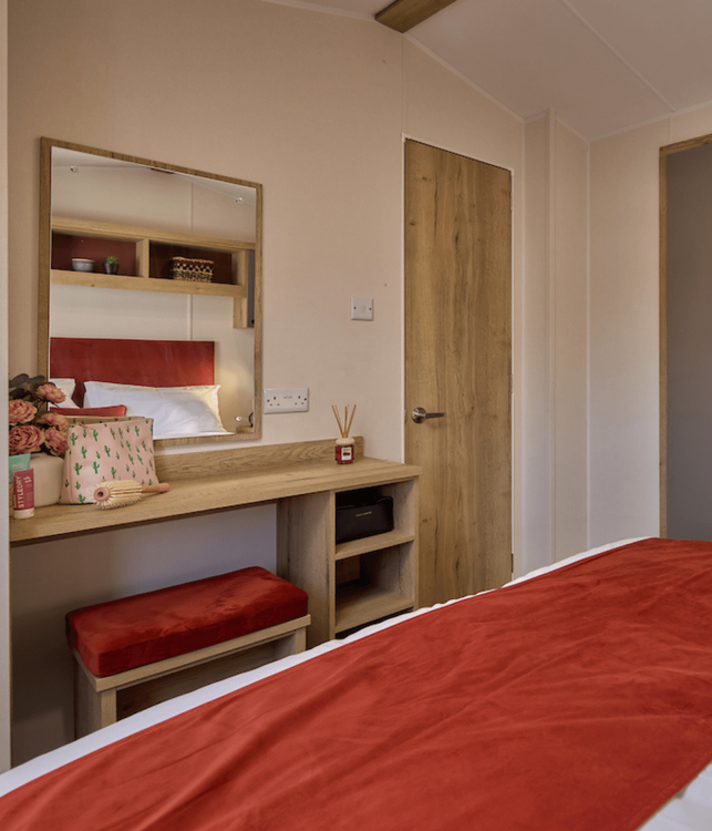 The Willerby Rio master bedroom has dressing table in an oak effect with storage and an upholstered orange chair which matches the colour of the home.