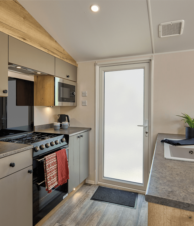 The Willerby Rio kitchen and dining area has oak effect kitchen storage units with light grey cupboards and worktops.