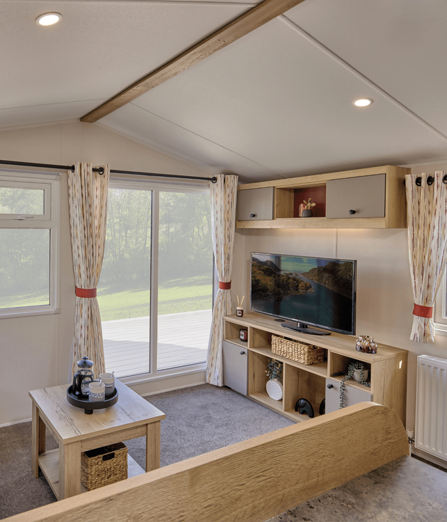 The Willerby Rio lounge has a fixed cream corner sofa with an optional orange armchair, and has a oak effect media unit with light grey cupboard doors with a matching coffee table.