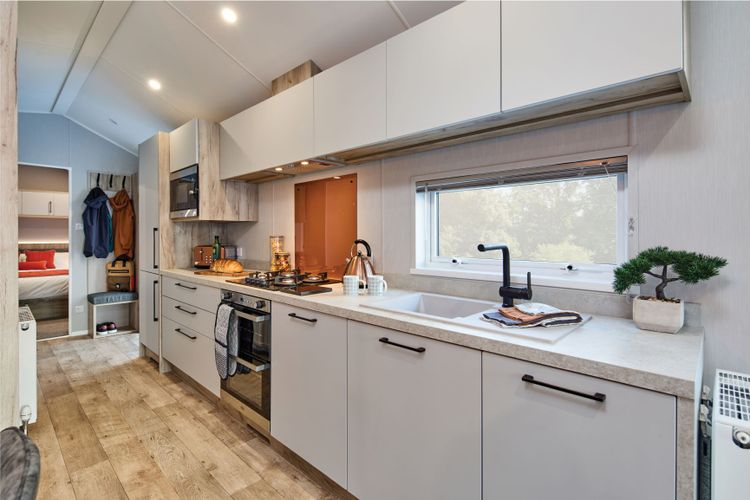 The Willerby Astoria stylish linear kitchen with white cupboard doors and an orange splashback.