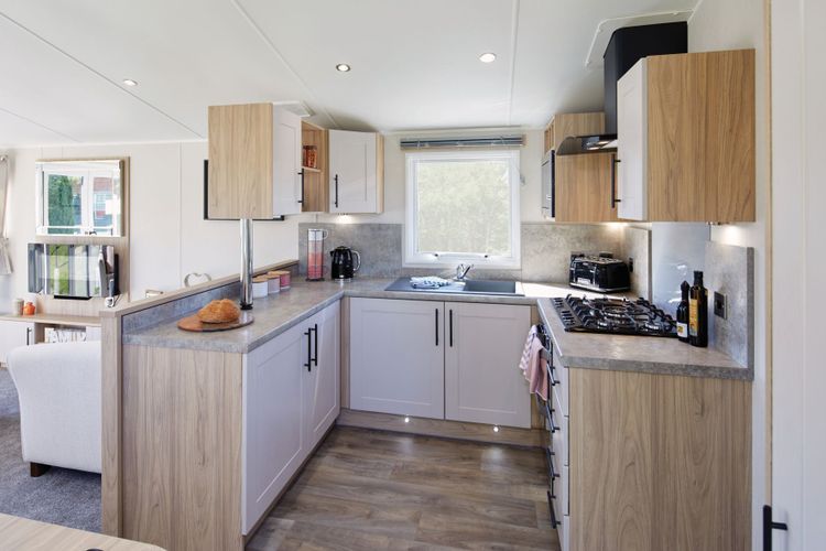 The Willerby Manor C-shaped kitchen has white cupboard doors on oak effect units and grey worktops.