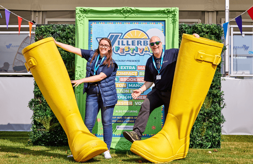 Two Willerby team members pose with giant yellow wellies at the Great Caravan, Motorhome and Holiday Home Show. The sun is out and they are smiling