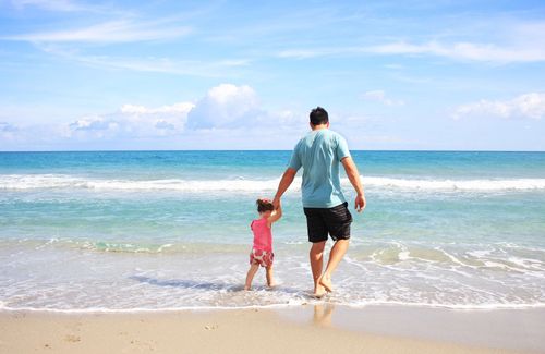 Father and daughter paddling in the sea under blue skies on holiday