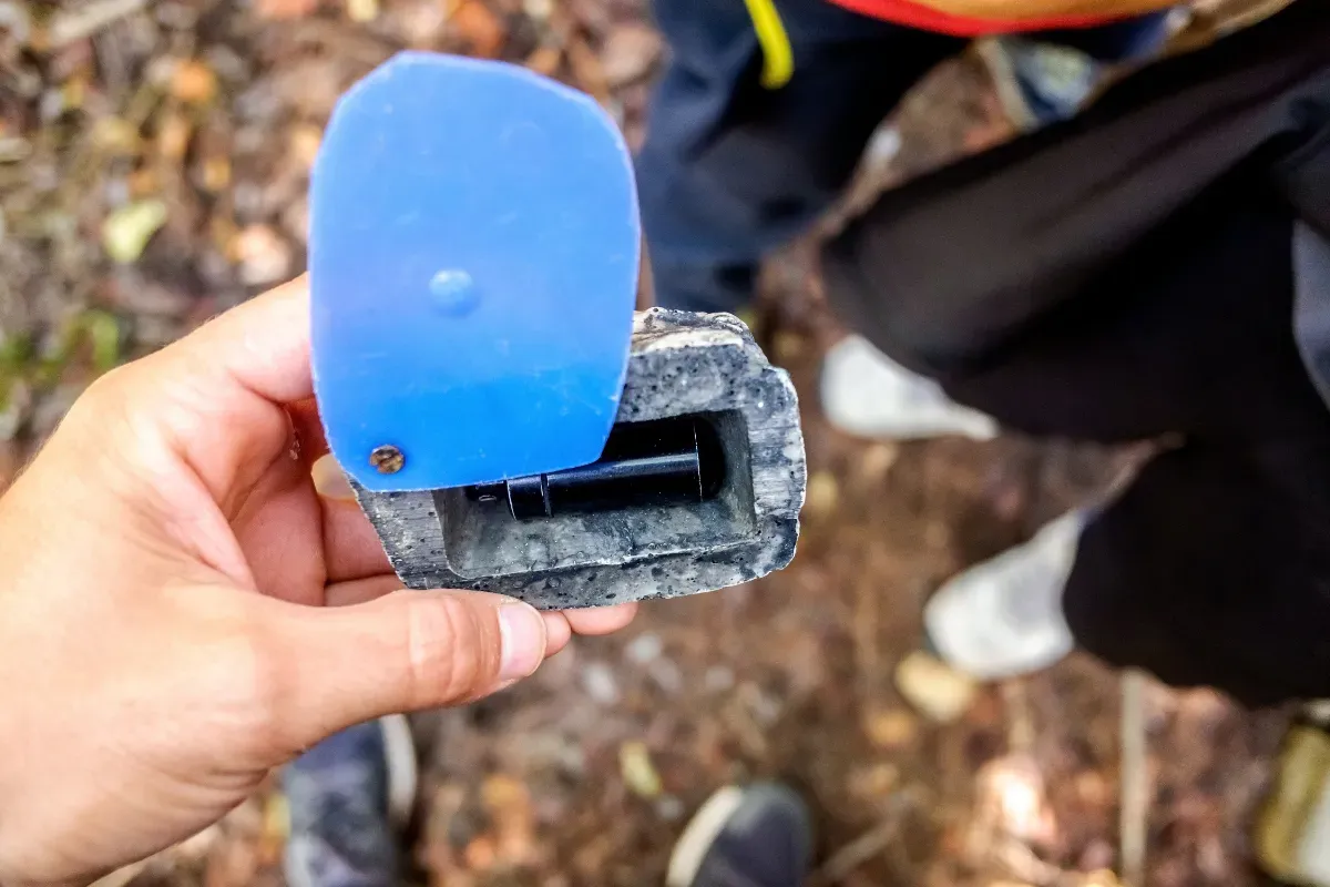 Hand holding a found geocache, opened to show the sealed container inside